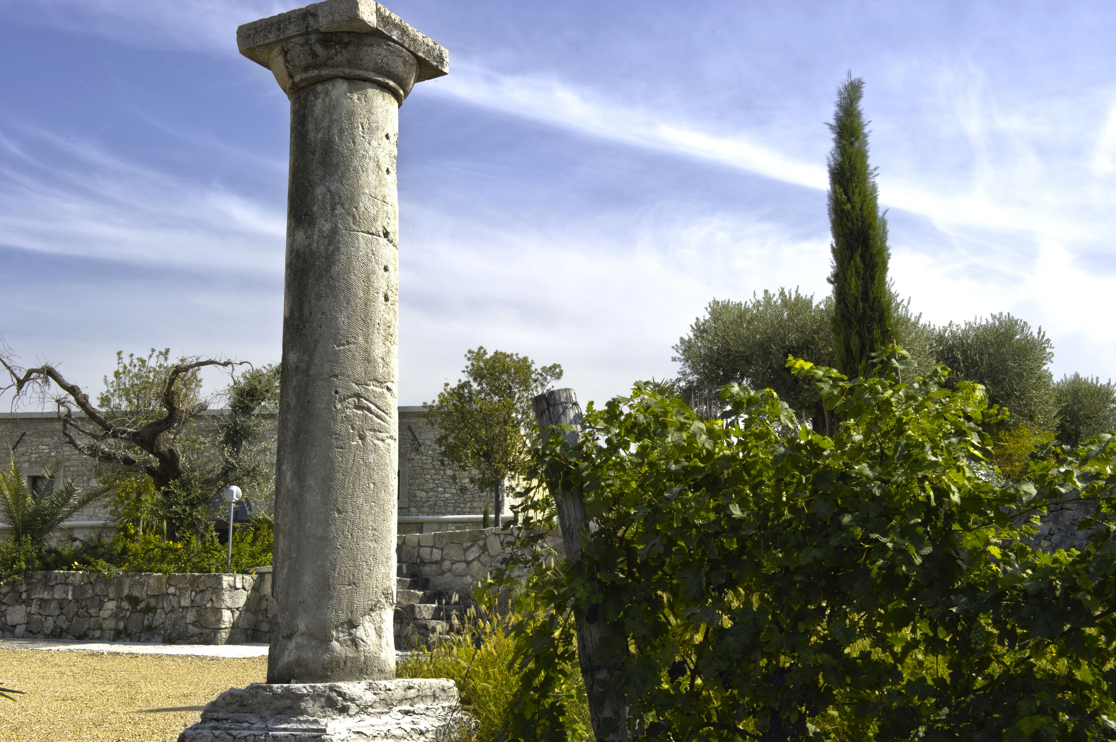 Un columnario de piedra en un jardín, con un muro de piedra y árboles al fondo.