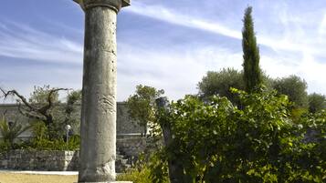 Un columnario de piedra en un jardín, con un muro de piedra y árboles al fondo.
