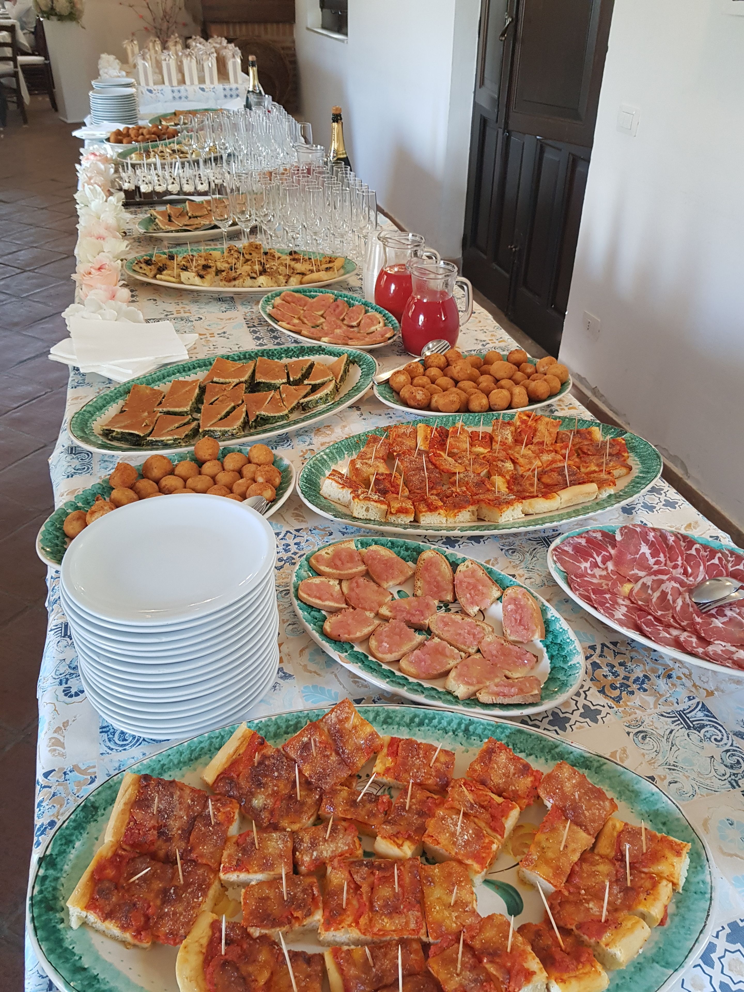 Une table de buffet proposant divers plats, notamment des pizzas, des pâtisseries et des plateaux de viandes, disposés sur une nappe à motifs.