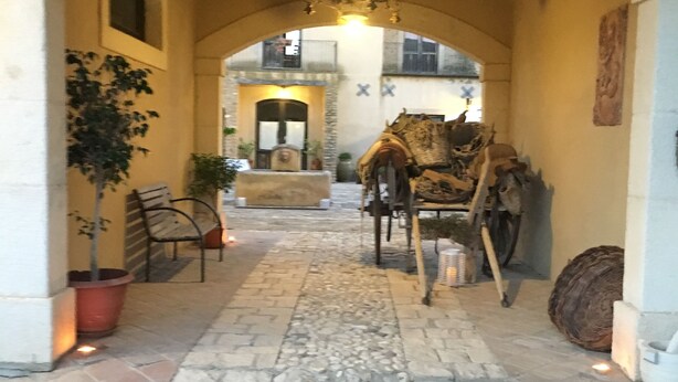 Un corredor abovedado con suelo de piedra, un candelabro y una silla de madera rústica.