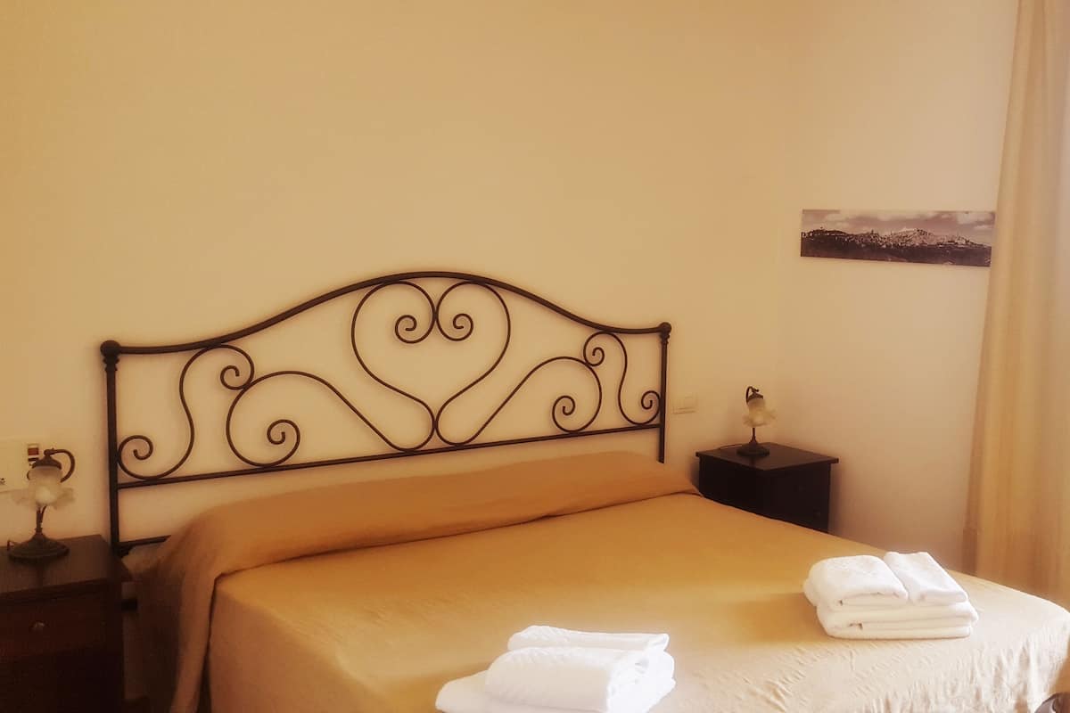 A neatly made bed with a metal headboard, a small bedside table with a lamp, and a framed picture on the wall.