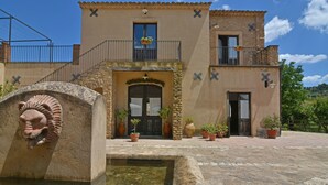 Un edificio con fachada de piedra, una entrada central con un arco decorativo y un pequeño patio con una fuente.