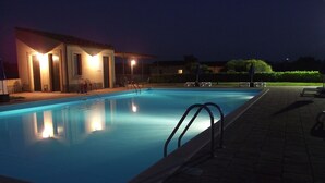 Una piscina por la noche con luces alrededor y un edificio al fondo.