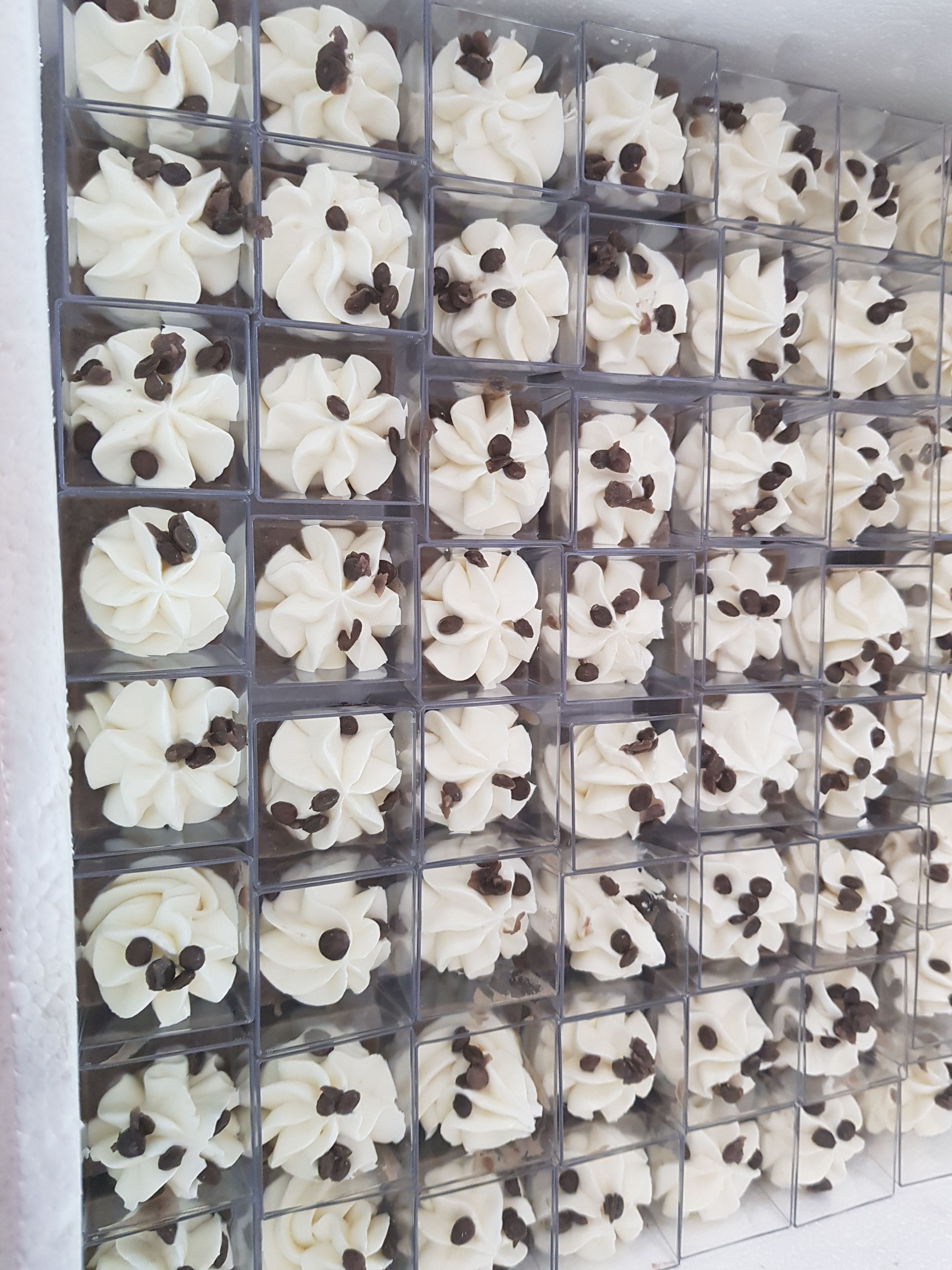 Un mur composé de compartiments carrés, chacun contenant un dessert blanc en forme de fleur, parsemé de pépites de chocolat.