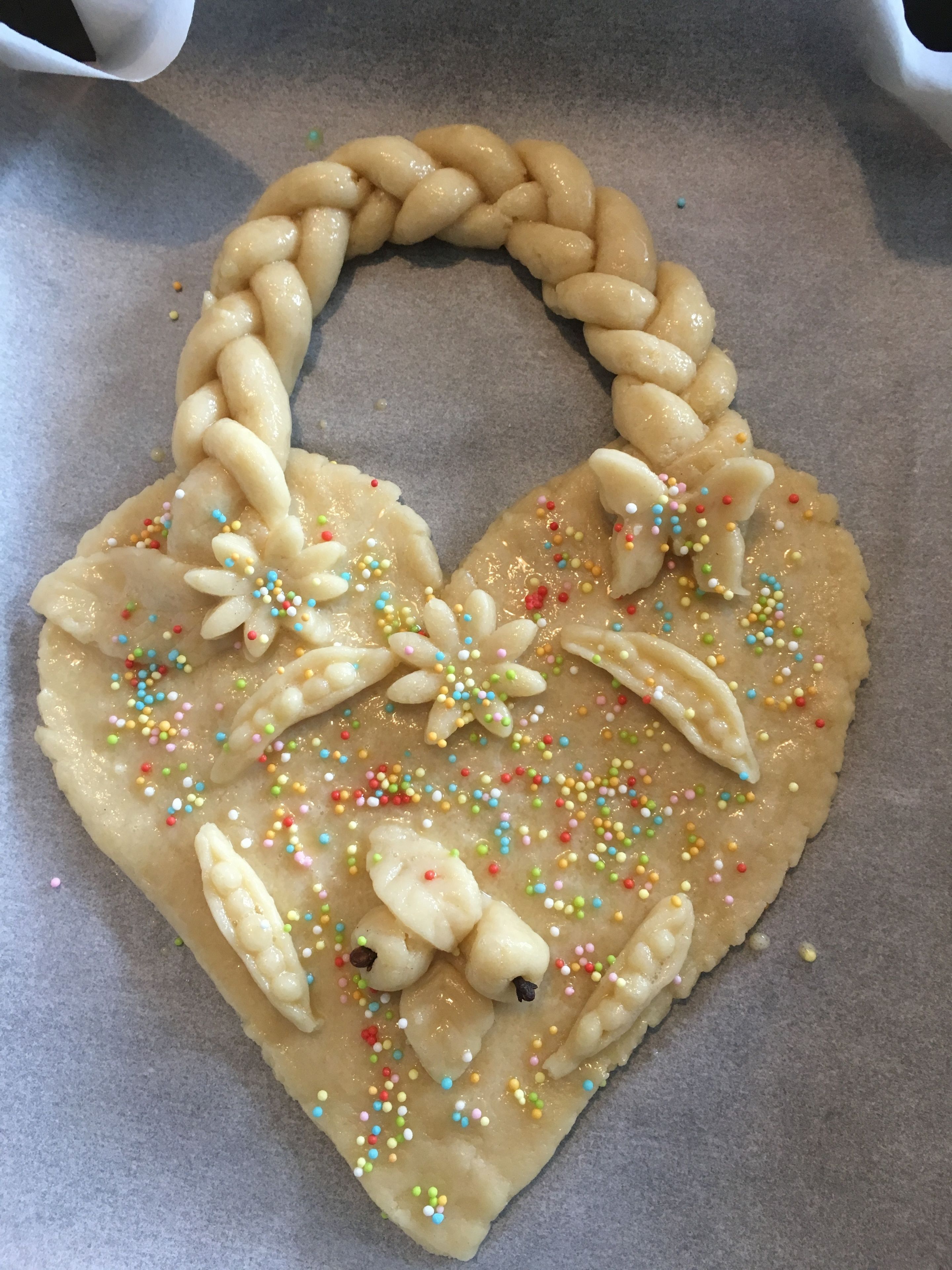 A heart-shaped pastry with colorful sprinkles and a braided handle, placed on parchment paper.