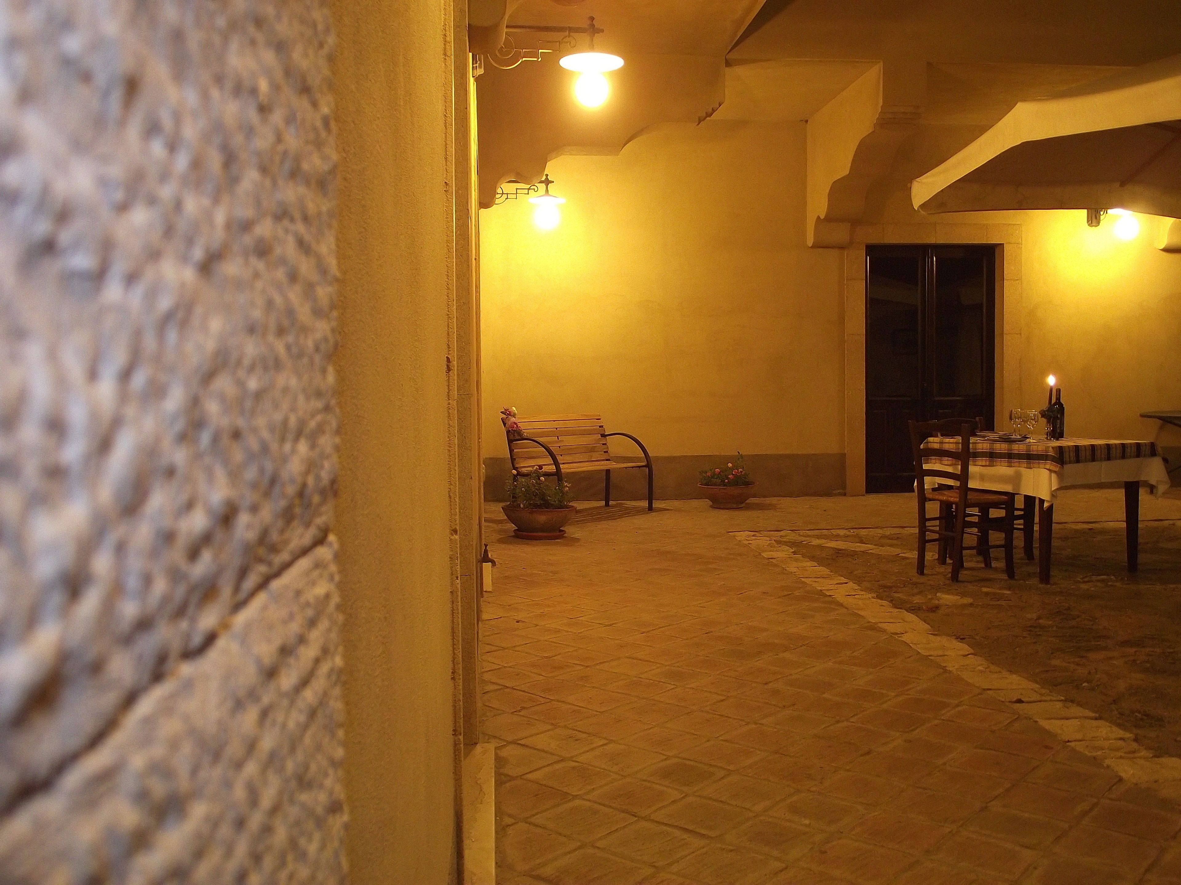Un patio extérieur à la lumière tamisée, avec une table dressée pour le repas, un banc et une plante en pot.