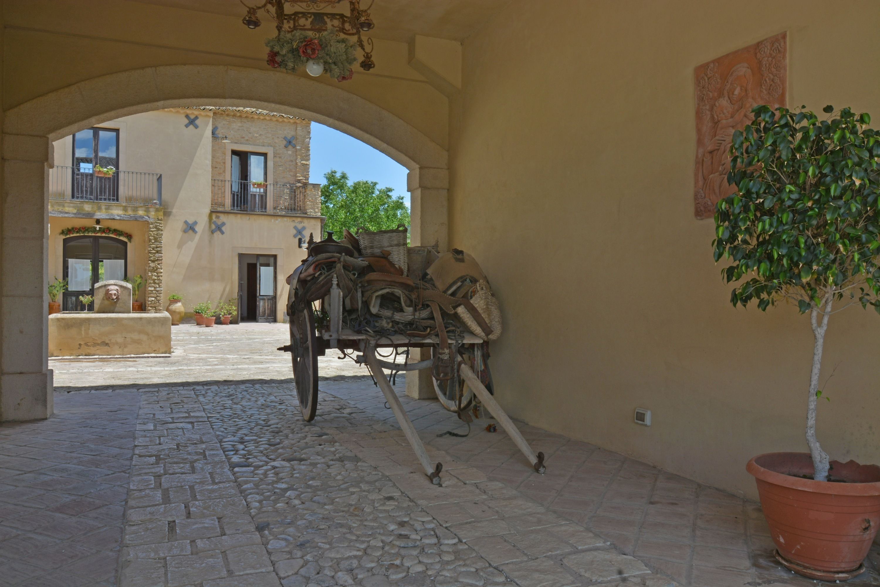 An interior courtyard with a stone floor, a potted tree, and a rustic cart.