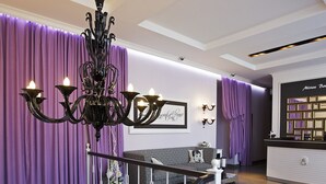 Un interior moderno con una escalera, una araña, cortinas moradas, un sofá a cuadros y un mostrador de recepción.