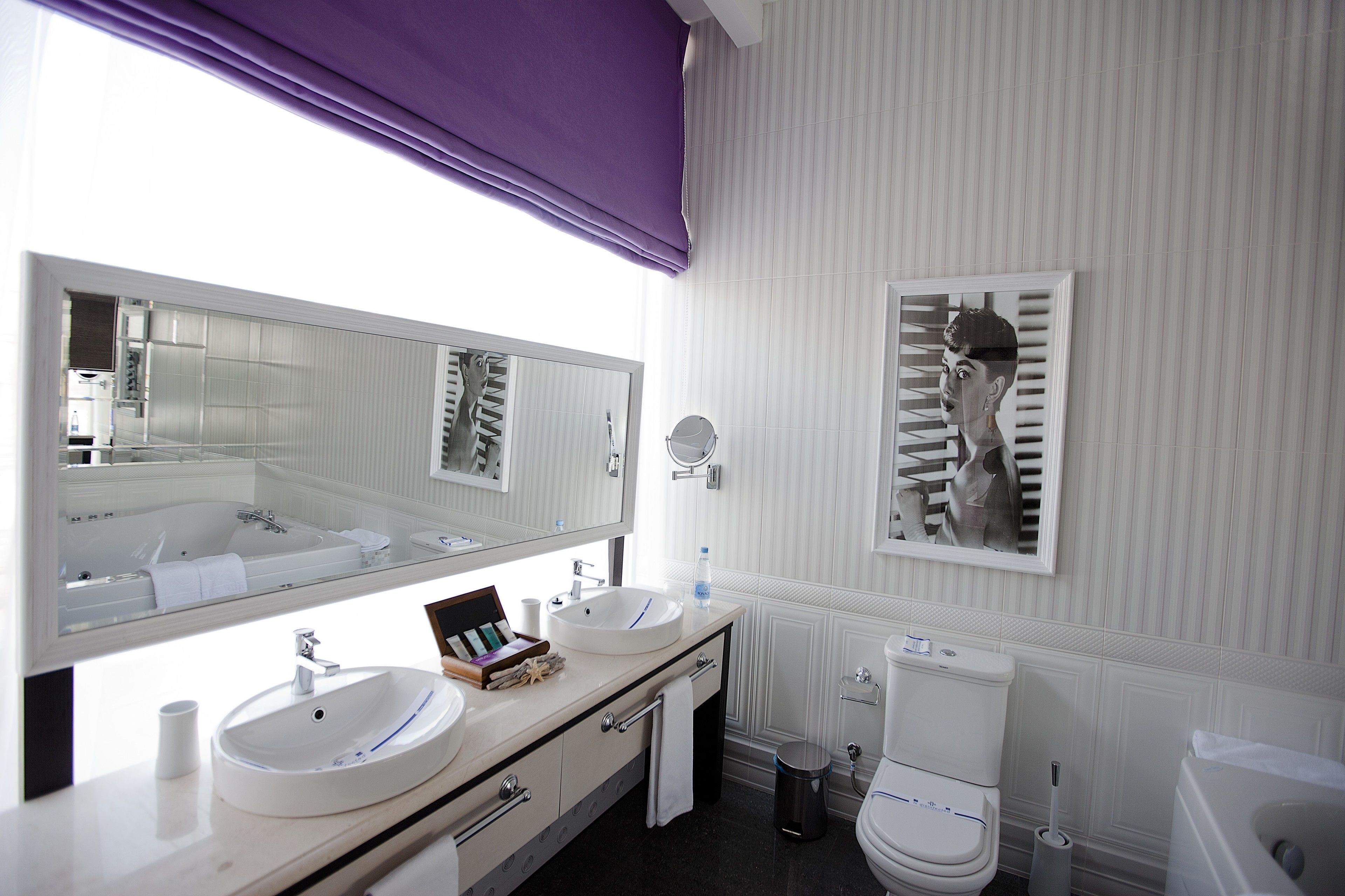Une salle de bain moderne avec un grand miroir, deux lavabos, des toilettes et une poubelle.