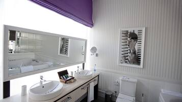 Une salle de bain moderne avec un grand miroir, deux lavabos, des toilettes et une poubelle.