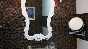 Ein Badezimmer mit einem weißen Waschbecken, einem großen, verzierten Spiegel und zwei Wandleuchten mit roten Lampen.