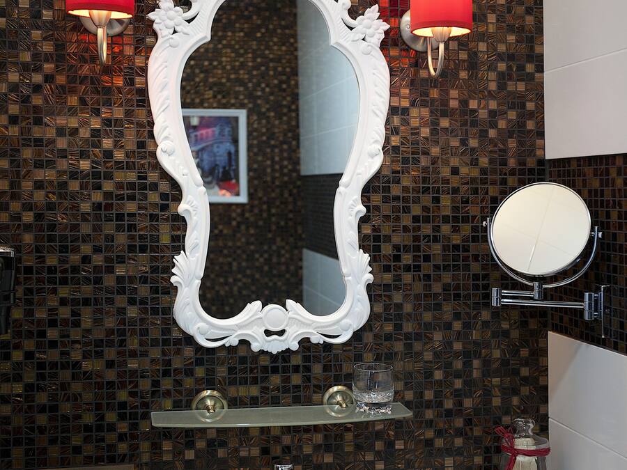 Ein Badezimmer mit einem weißen Waschbecken, einem großen, verzierten Spiegel und zwei Wandleuchten mit roten Lampen.