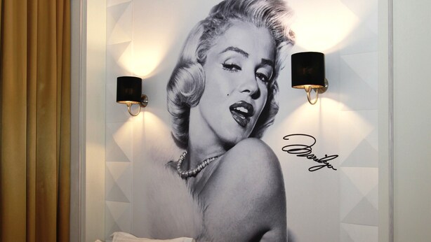 Un dormitorio con un mural grande, una cama con muchos cojines y dos lámparas de pared.