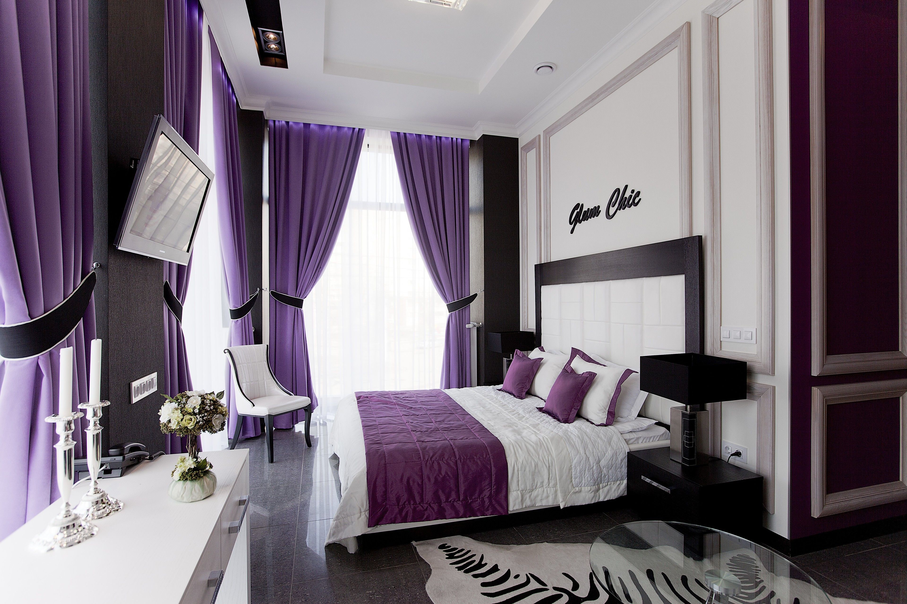 A modern bedroom with a large bed, a bedside table, a chair, and a flat-screen TV mounted on the wall.