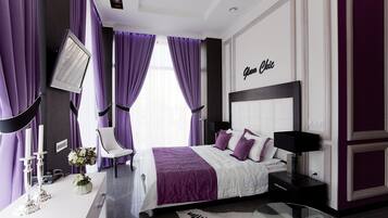 A modern bedroom with a large bed, a bedside table, a chair, and a flat-screen TV mounted on the wall.