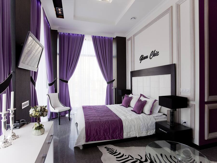 A modern bedroom with a large bed, a bedside table, a chair, and a flat-screen TV mounted on the wall.