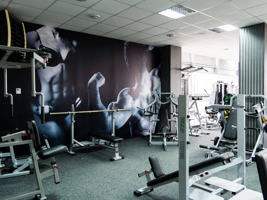 A gym with various exercise equipment, a large mural on the wall, and a ceiling with fluorescent lights.