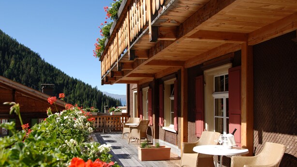 A wooden building with a balcony, outdoor seating, and a view of a forested mountain.