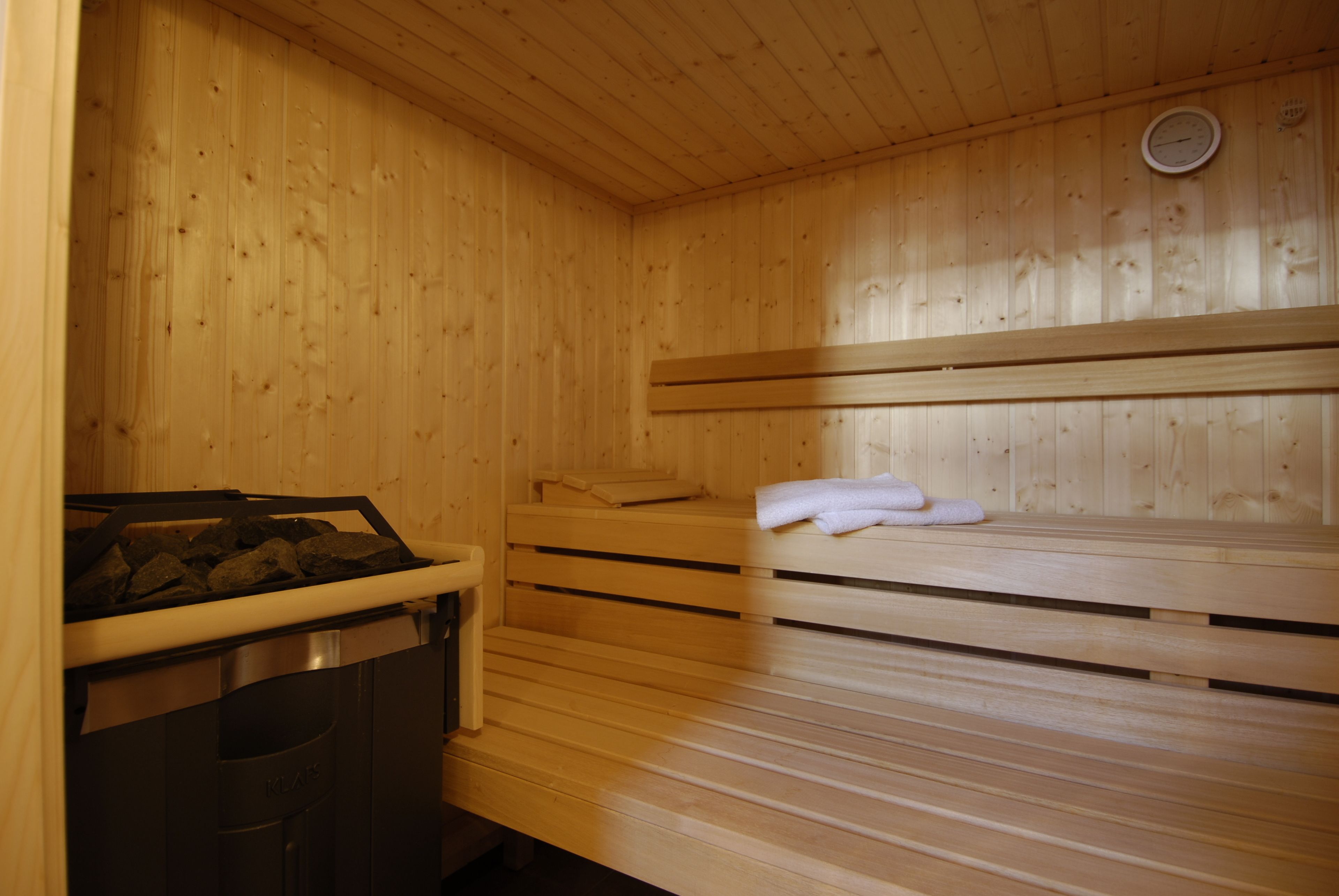 A sauna room with wooden benches, a bench heater, and a towel rack.