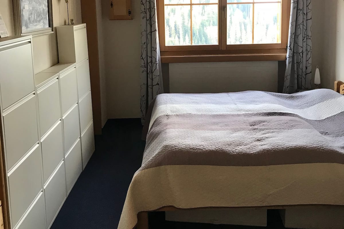 A bedroom with a bed, a window with curtains, a dresser, and a framed picture on the wall.