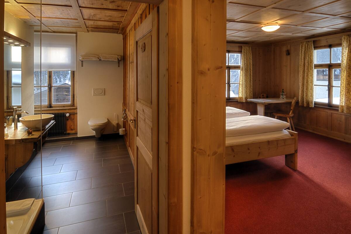 A wooden interior with a bathroom, a bed, and a small table.