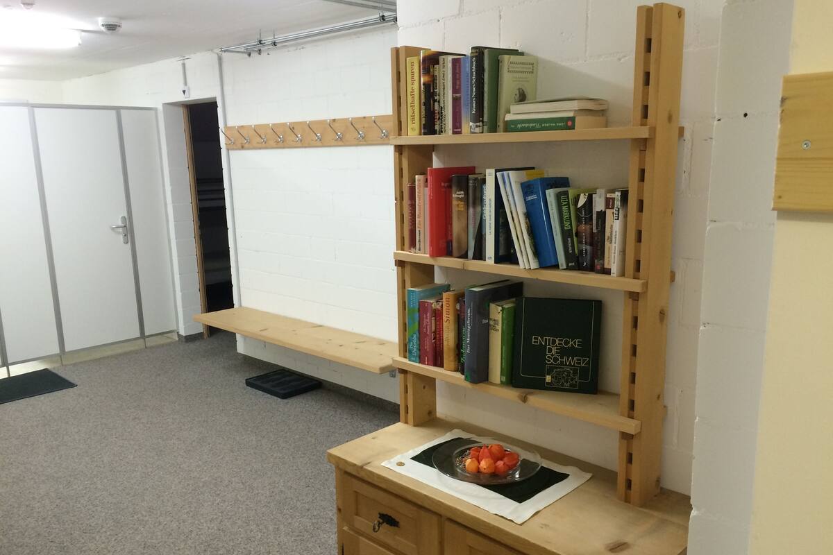 A room with a wooden bookshelf filled with books, a small wooden table with a bowl of fruit, and a door in the background.