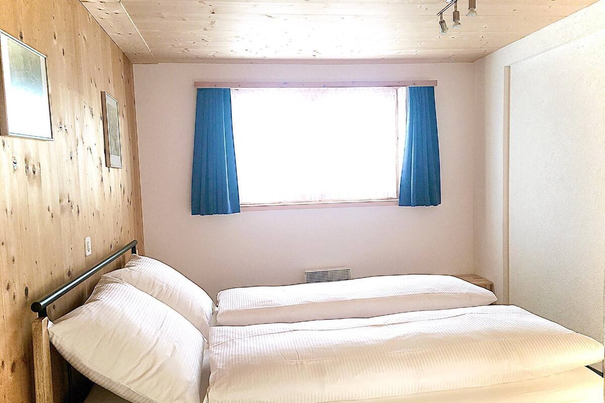 A room with a bunk bed, wooden walls, a window with blue curtains, and a small radiator.