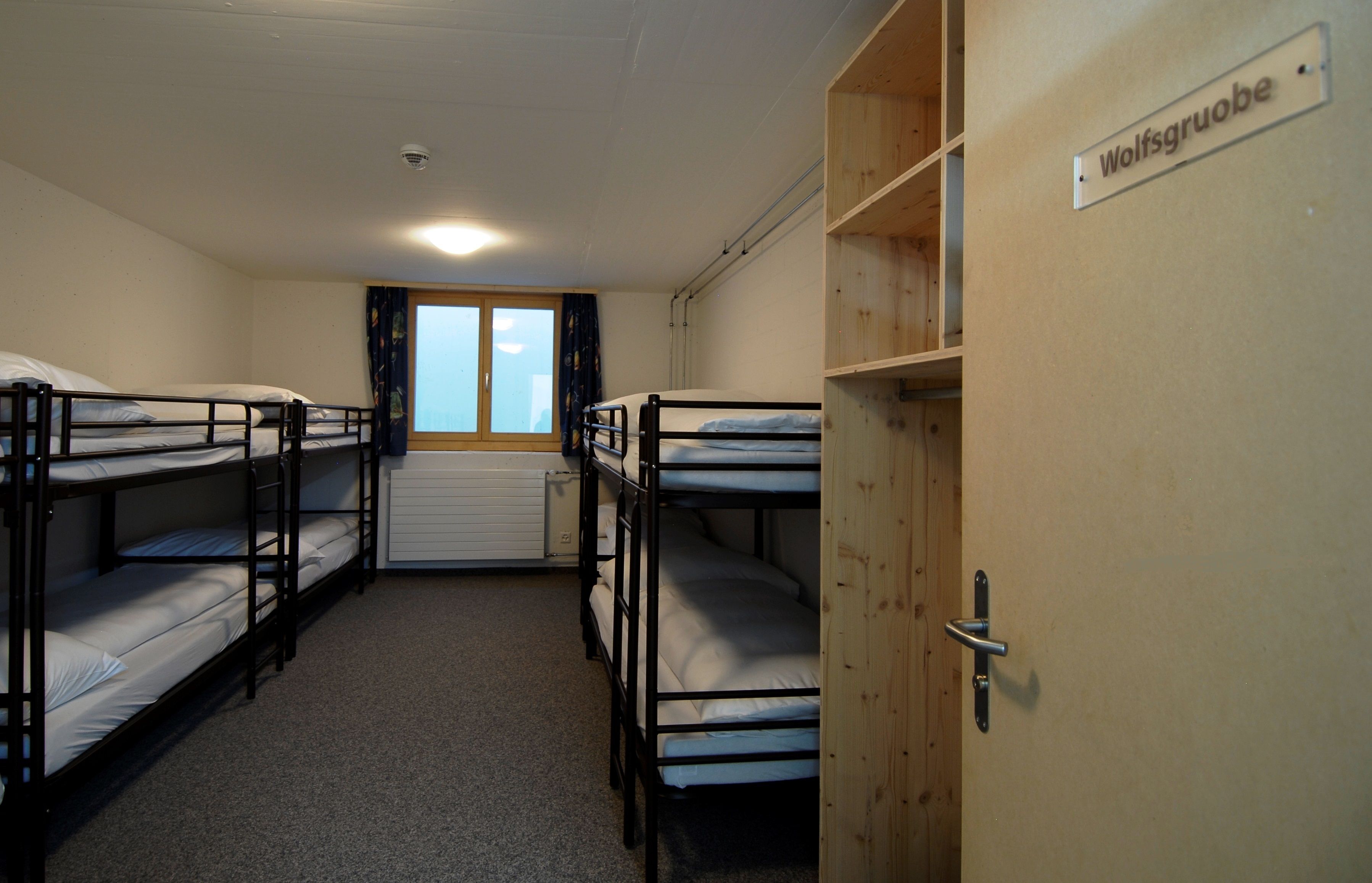 Un dormitorio con literas, una puerta de madera con la leyenda 'Wolfsgruove' y una ventana con cortinas.