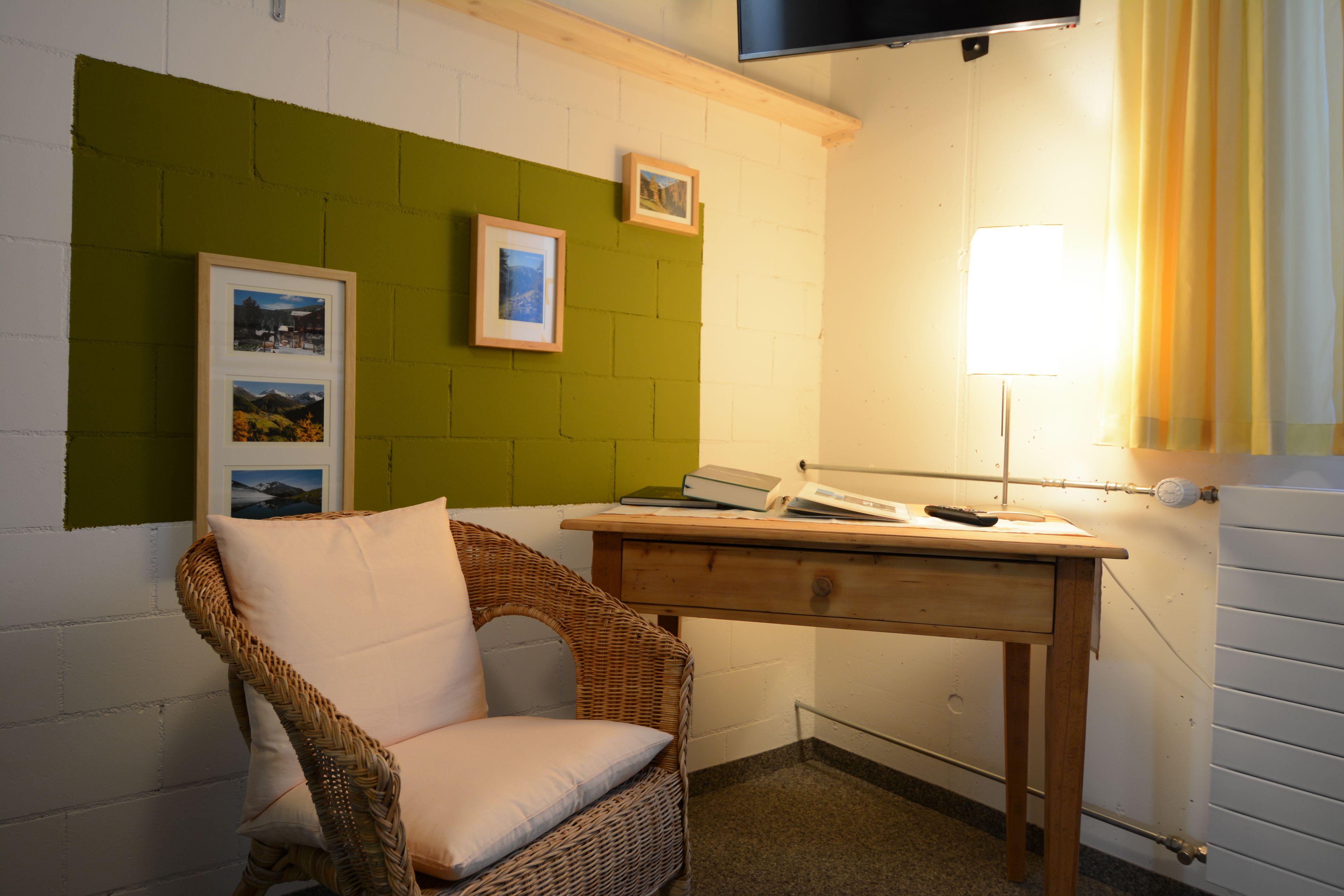 A room with a wicker chair, a wooden desk, and a green accent wall.