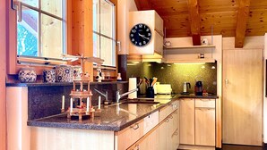 A kitchen with wooden cabinets, a granite countertop, a clock, and a window with a view of the outdoors.