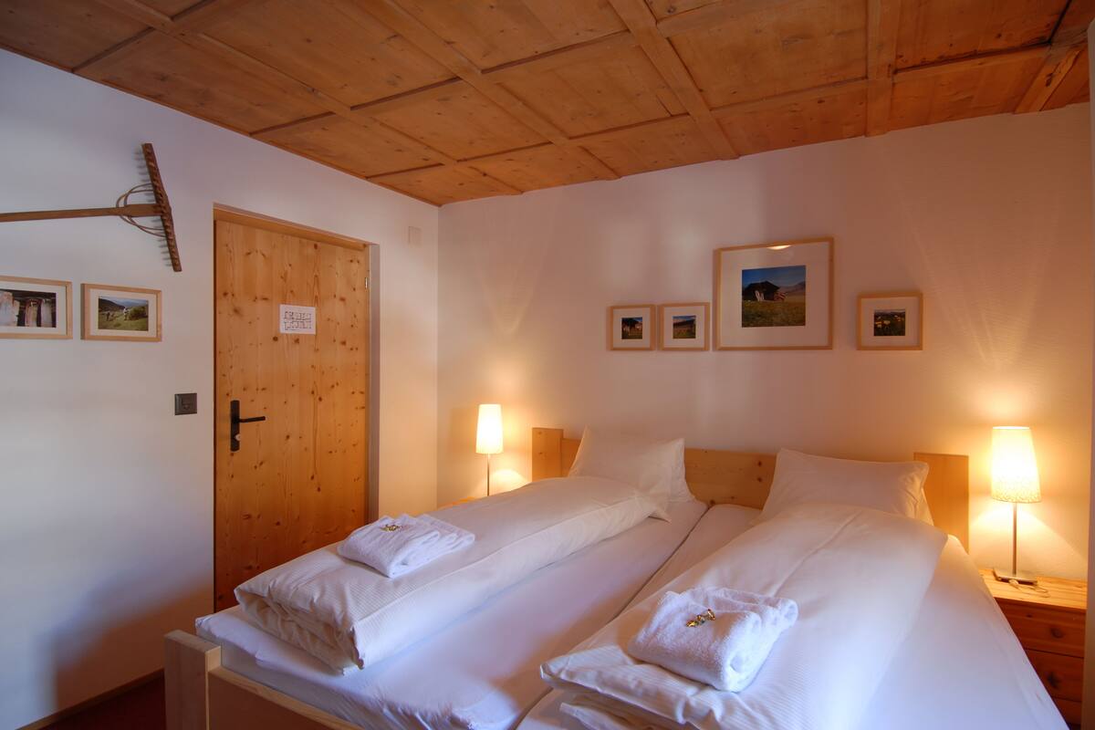 A double room with two beds, wooden ceiling, and framed pictures on the wall.