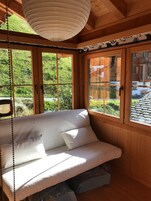 A wooden cabin with a bed, large windows, and a hanging light fixture.