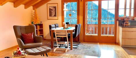 A cozy loft-style room with a wooden ceiling, a dining area with a table and chairs, a fireplace, and a view of a snowy mountain through large windows.