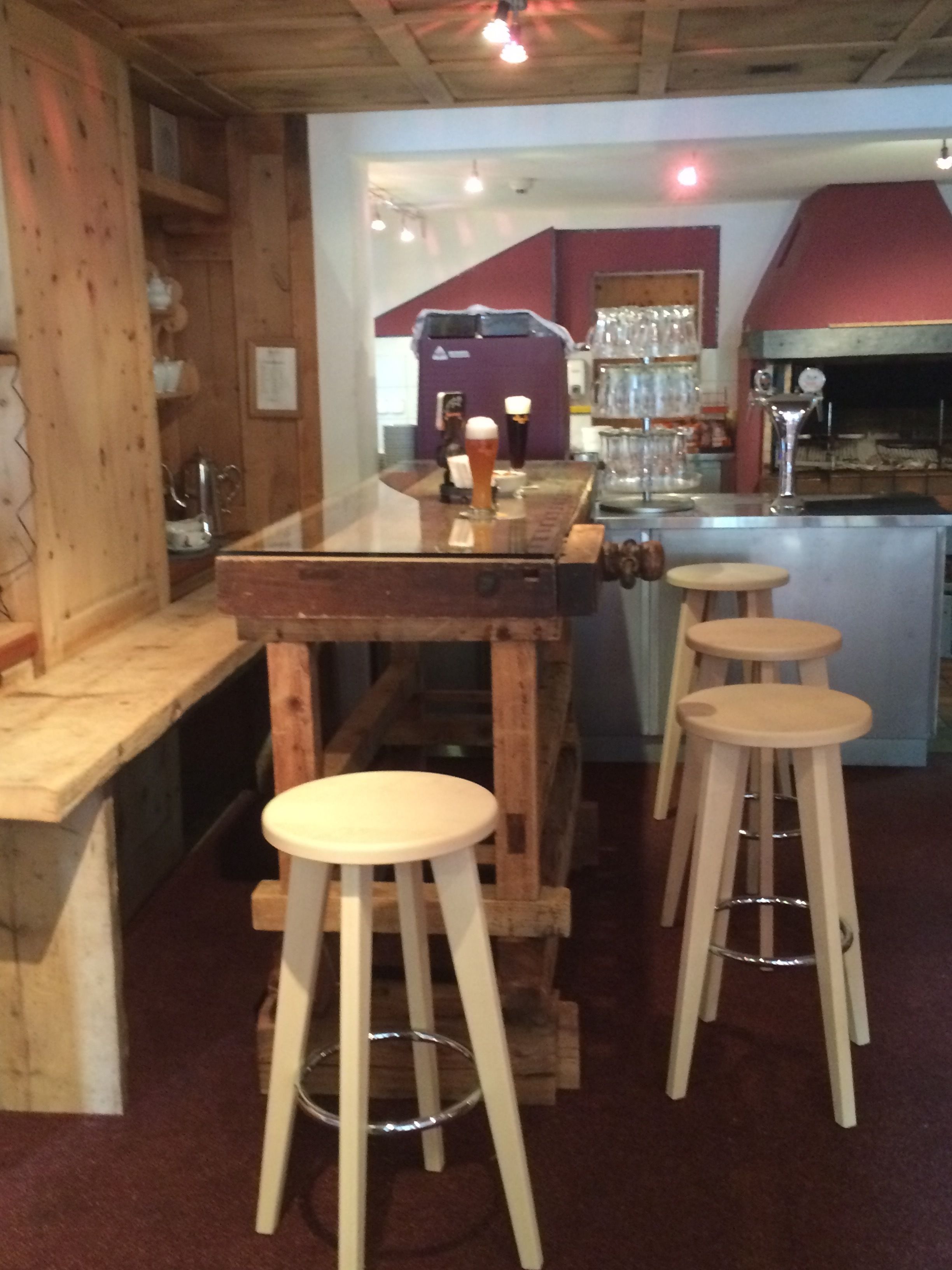 Un coin bar au style rustique, avec des tabourets en bois, un comptoir et une variété de verres.
