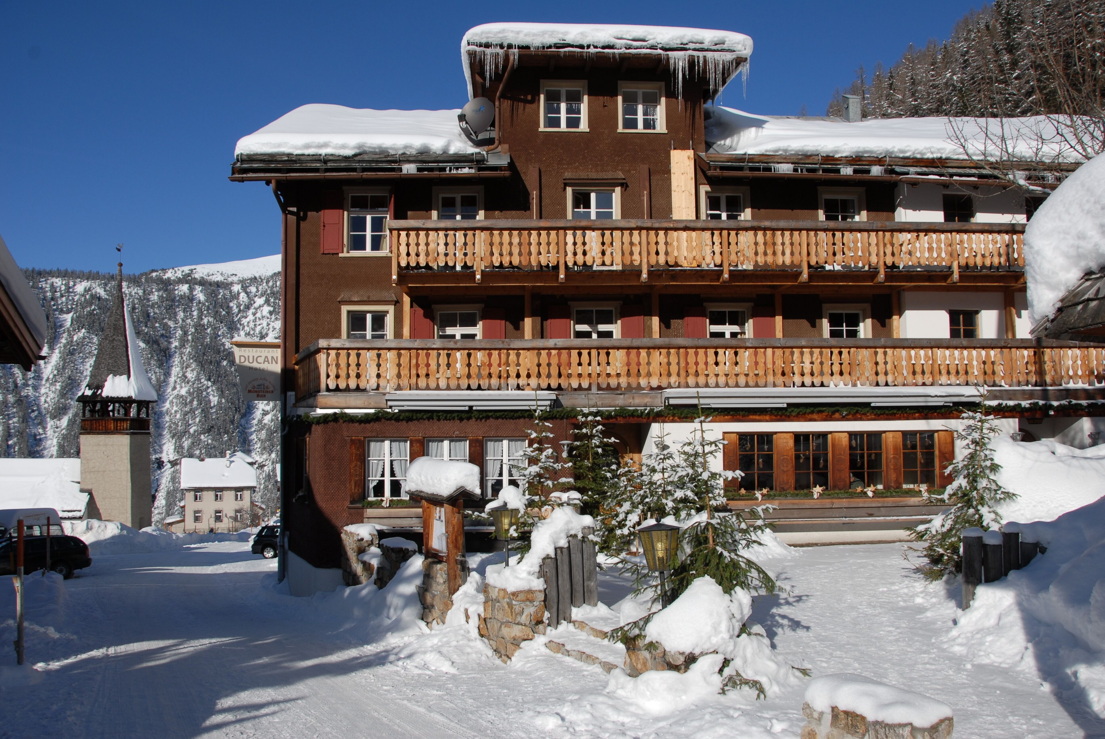 A multi-story hotel with balconies, a snow-covered roof, and a mountainous backdrop.