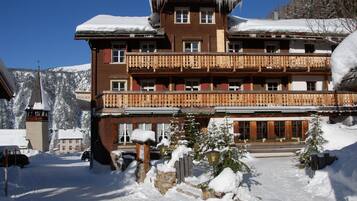 A multi-story hotel with balconies, a snow-covered roof, and a mountainous backdrop.