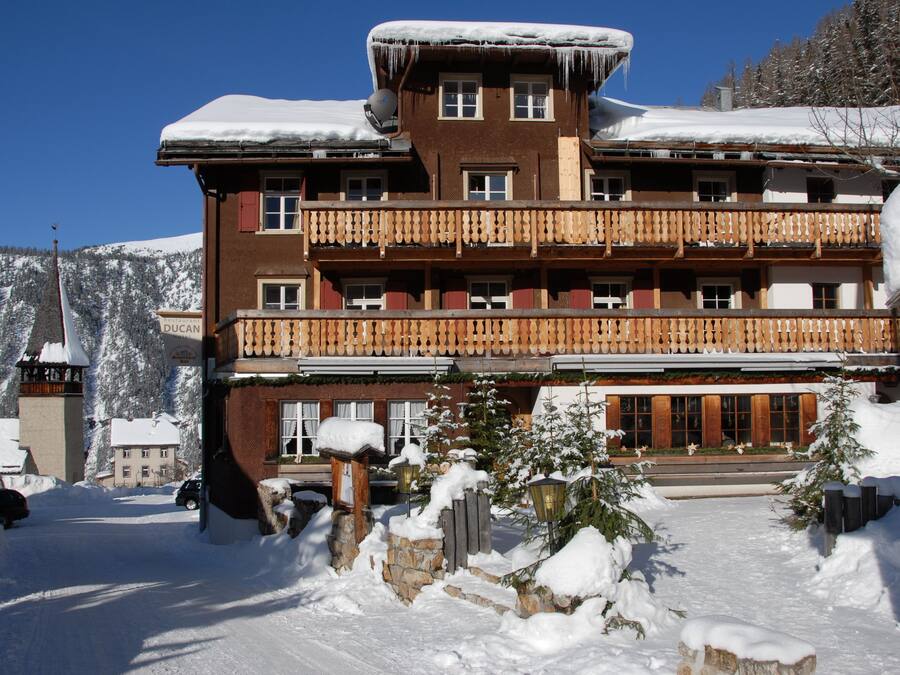 A multi-story hotel with balconies, a snow-covered roof, and a mountainous backdrop.