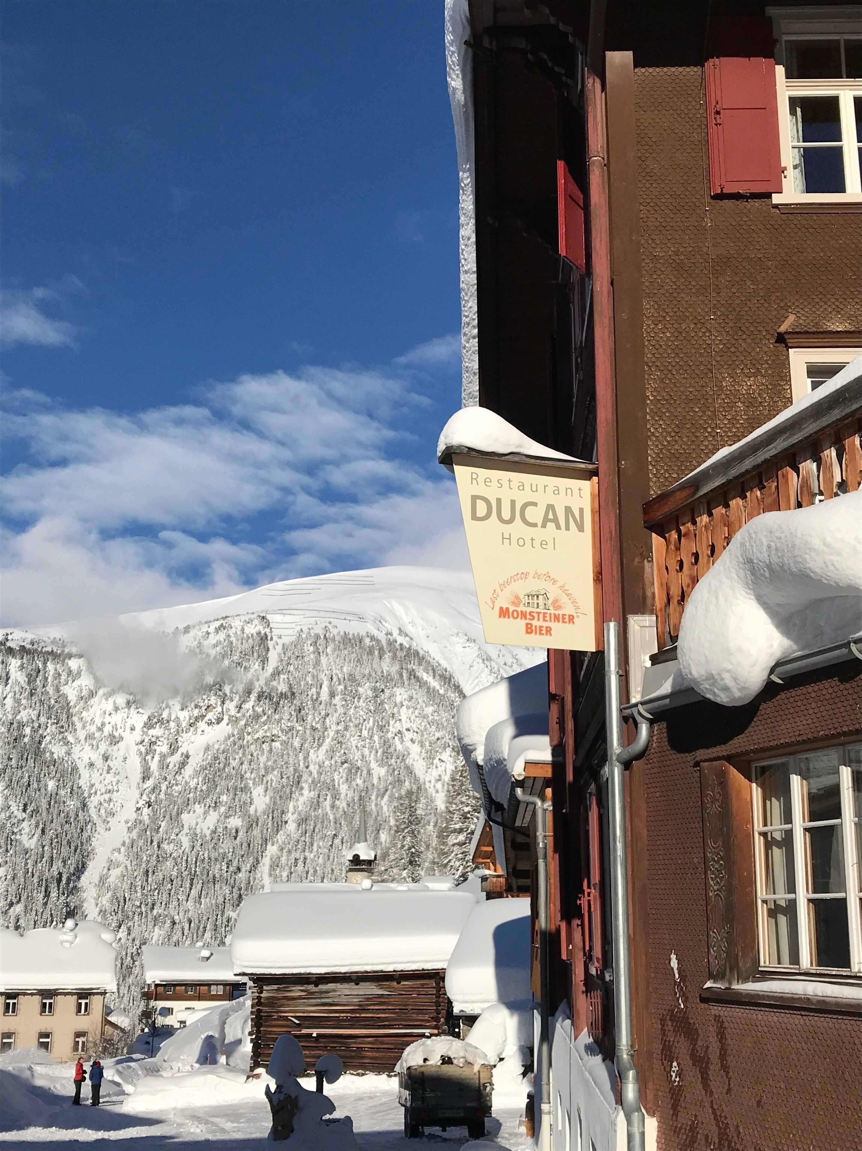 A sign for the DUCAN Hotel with a view of snow-covered mountains in the background.