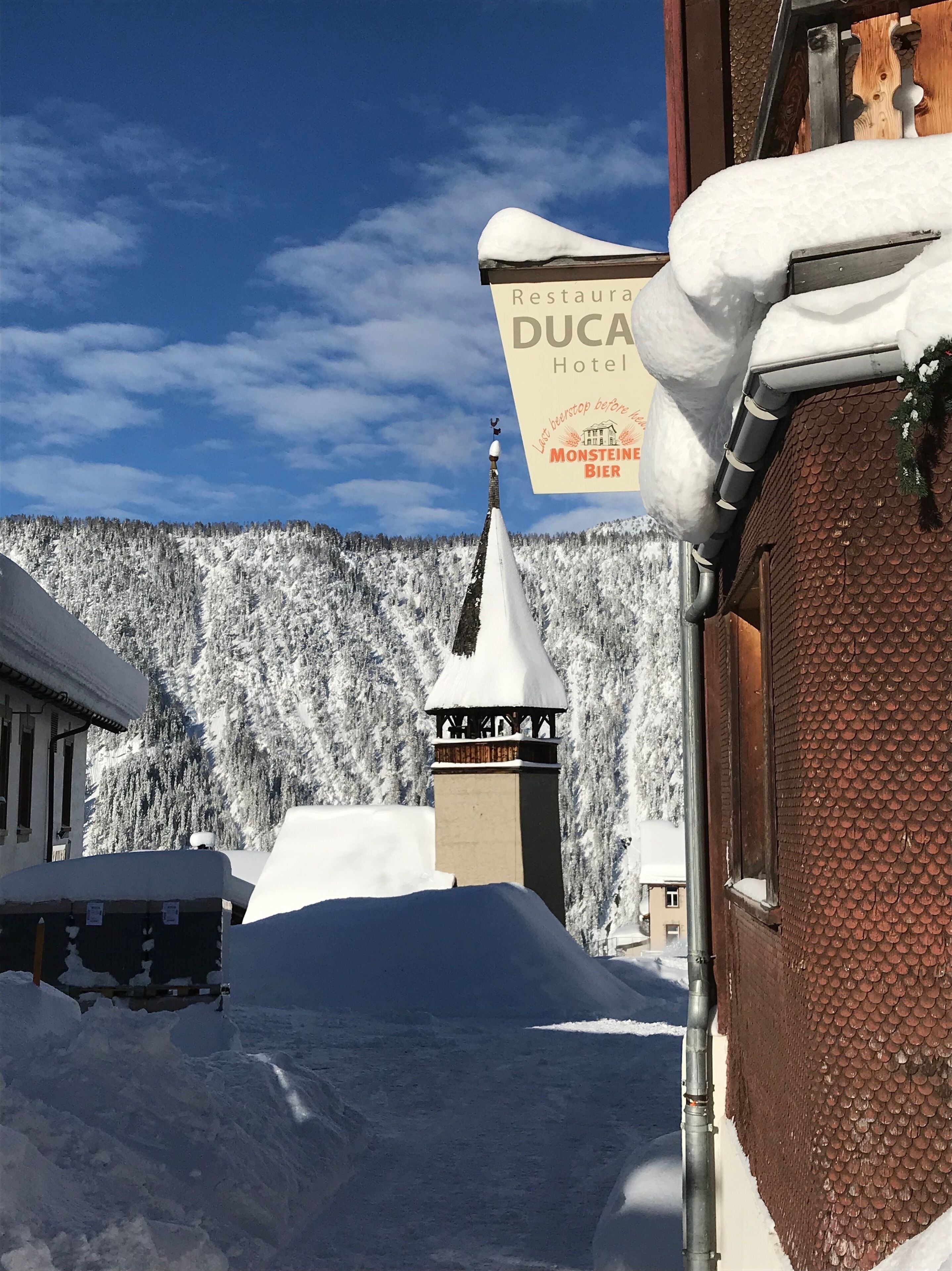 A snow-covered building with a sign for 'DUCA Hotel' and 'Monsteiner Bier'.