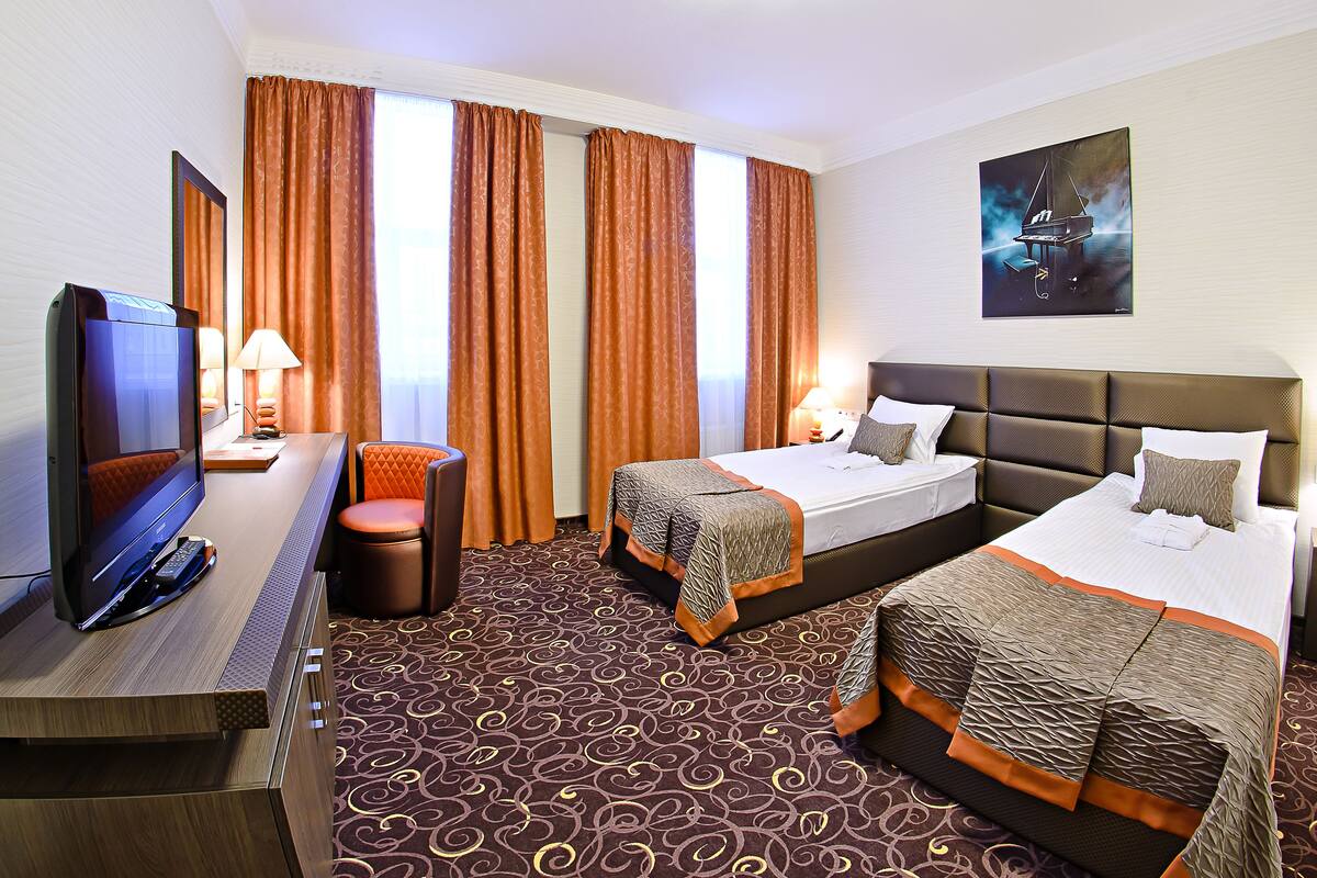 Ein Hotelzimmer mit zwei Betten, einem Schreibtisch mit Fernseher und einem Sessel.
