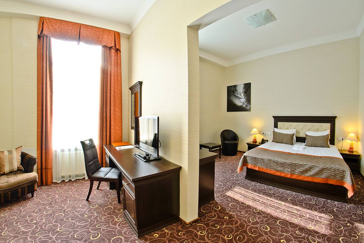 Ein Hotelzimmer mit einem Bett, einem Schreibtisch, einem Sessel, einem Fernseher und einem Bild an der Wand.