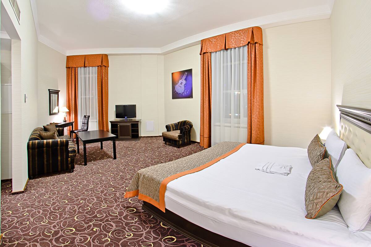 Ein Hotelzimmer mit einem großen Bett, einem Schreibtisch mit Stuhl, einem Fernseher und einem kleinen Sessel.