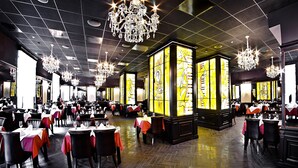 A spacious restaurant with high ceilings, chandeliers, and large stained glass windows. Tables are set with white tablecloths and red napkins. - ALFAVITO Kyiv Hotel (Kyiv)
