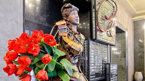 A statue of a woman holding a bouquet of red tulips, standing in a lobby with a black marble floor and a decorative metal gate in the background. - ALFAVITO Kyiv Hotel (Kyiv)
