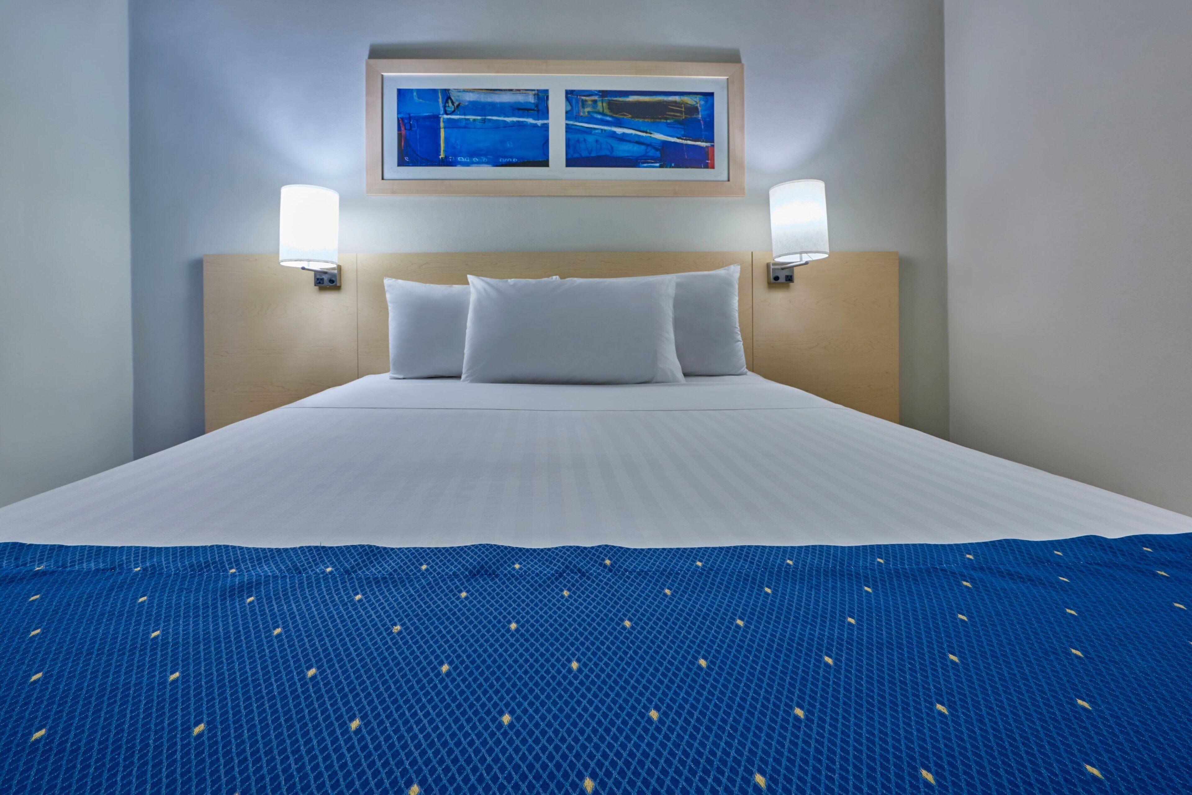 Habitación de hotel con una cama grande, dos lámparas de pared y una obra de arte enmarcada sobre la cama.