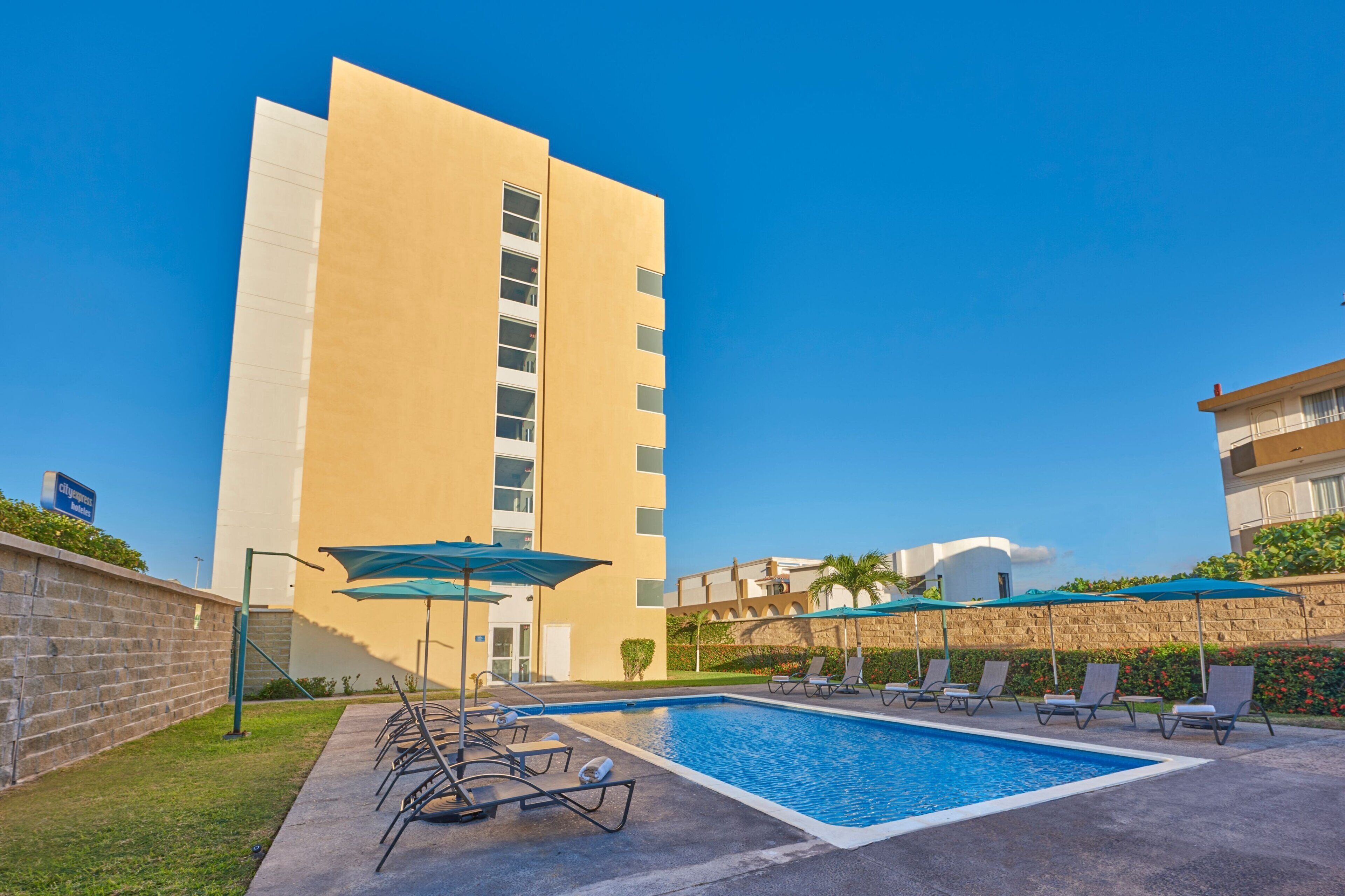 A hotel with a swimming pool, lounge chairs, and umbrellas.