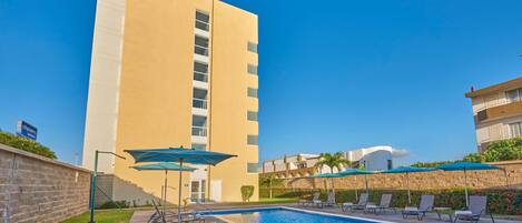 A hotel with a swimming pool, lounge chairs, and umbrellas.