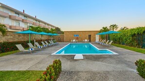 Ein Swimmingpool mit Liegestühlen und Sonnenschirmen, umgeben von einer Backsteinmauer und viel Grün.