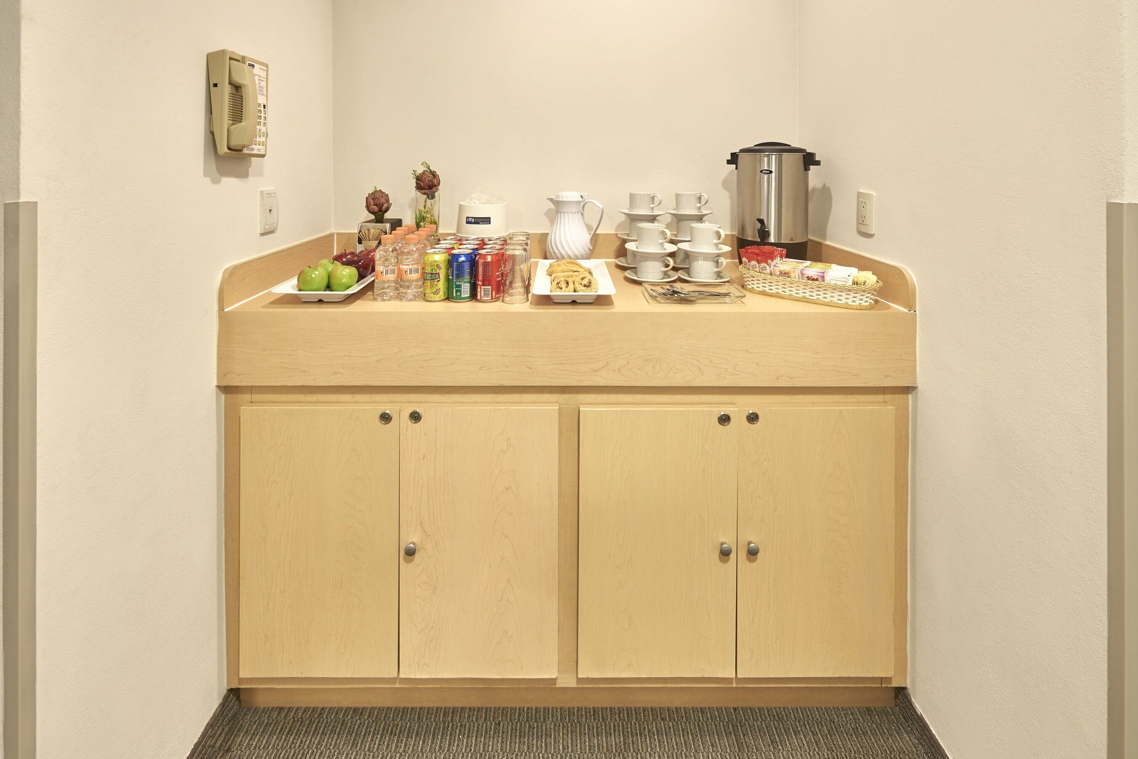 A kitchenette with a wooden countertop, cabinets, a coffee maker, a kettle, and various food items.