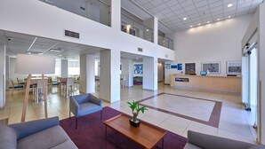 Eine geräumige Lobby mit einer Rezeption, einer Sitzecke und einer Treppe, die zwei Ebenen verbindet.